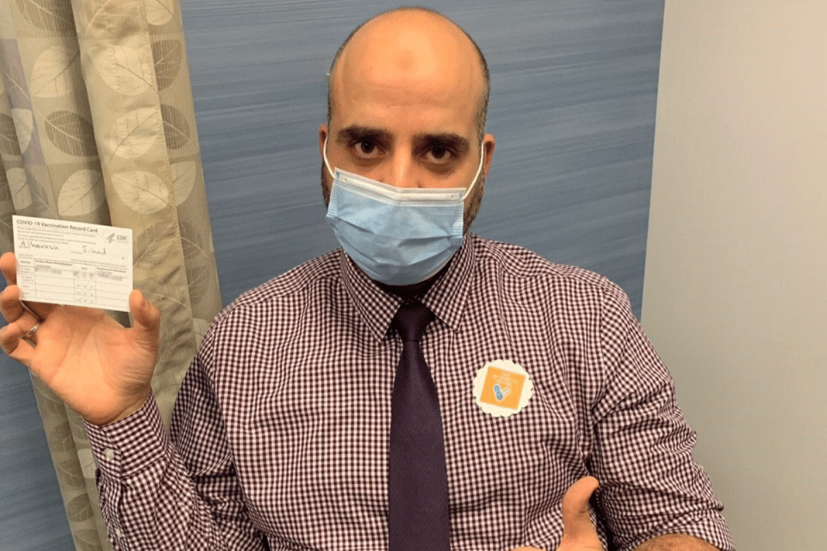 Man holding vaccination card with "I got vaccinate" sticker on his chest